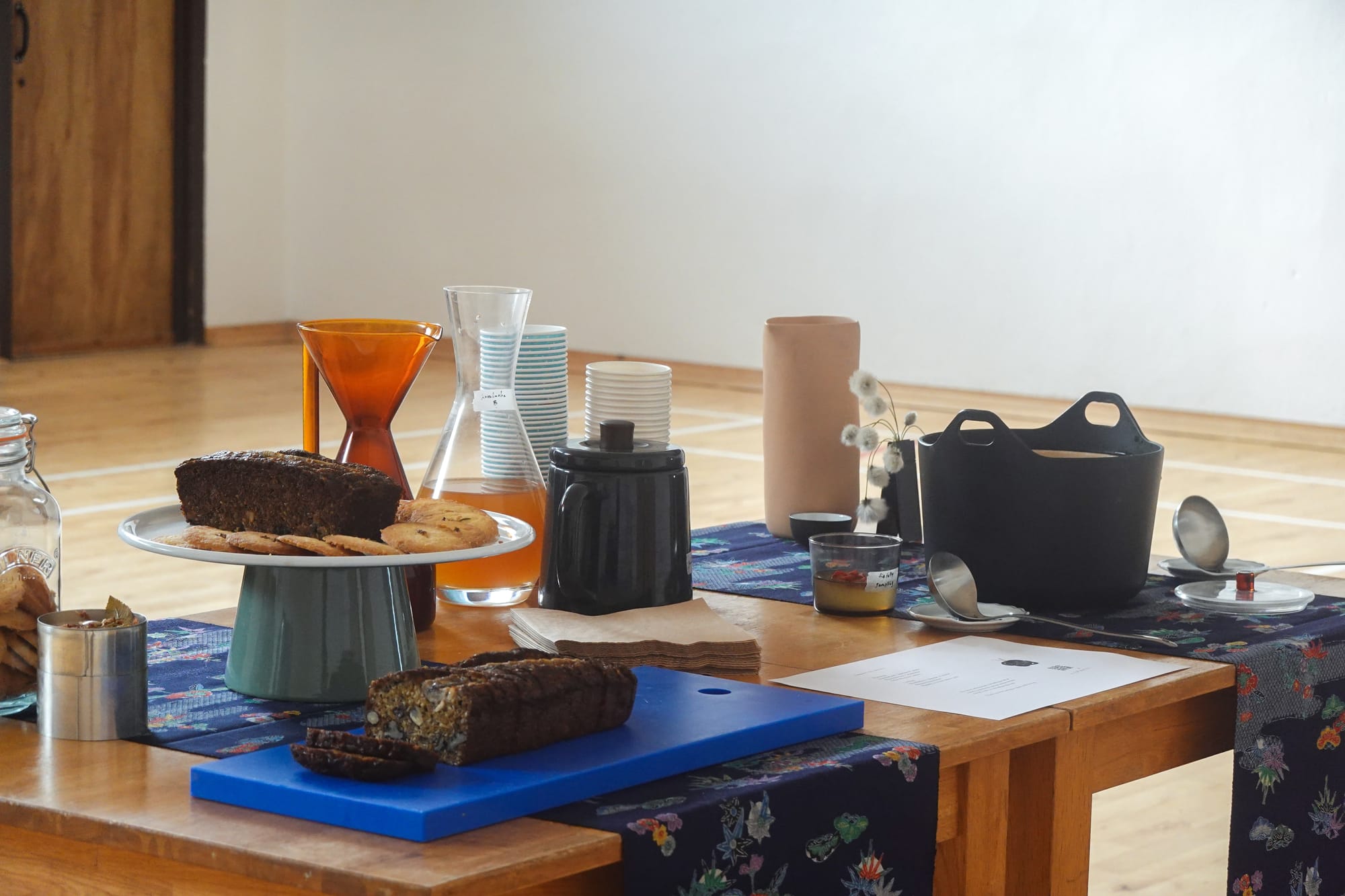 two tables put together with clothes on top, hosting a selection of cookies, bread, drinks